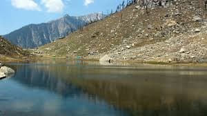 The Kareri Lake meadow and shoreline below the Dhauladhar wall